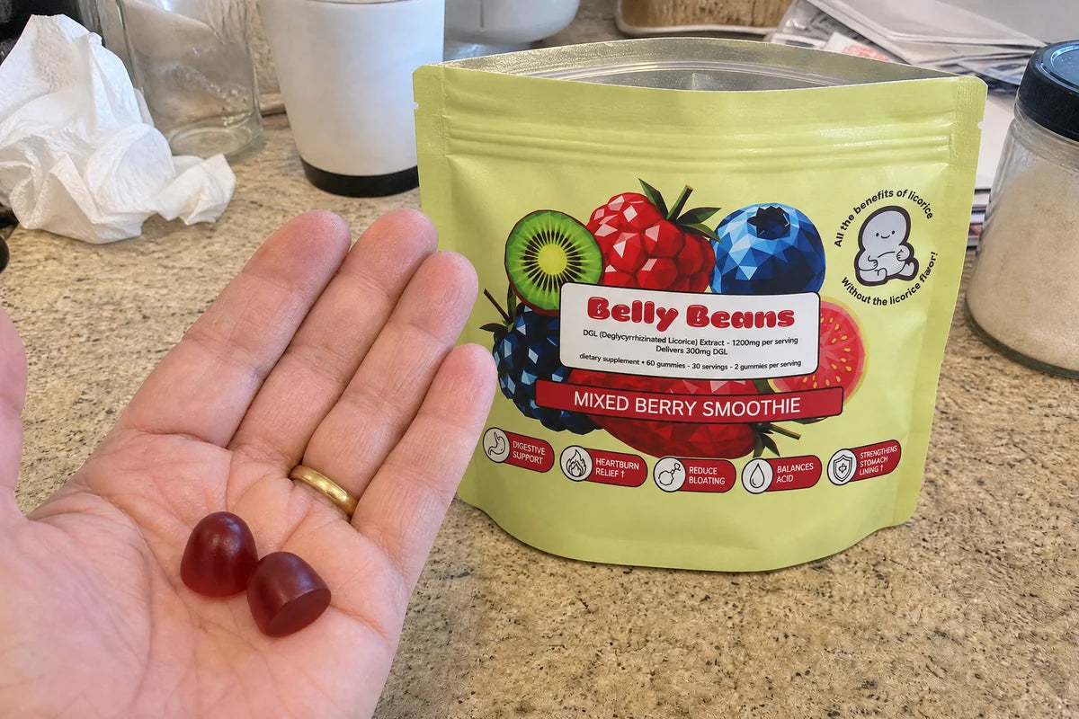 Two Belly Beans gummies in an open hand with the pouch on a kitchen counter